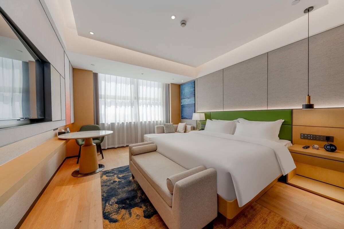 Et moderne hotelværelse med en stor seng, et lille bord, en sofa og et skrivebord med en lampe.