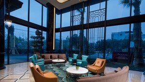 Un vestíbulo moderno con ventanas amplias, un área de descanso con sofás y sillones, y un cartel visible de Ramada.