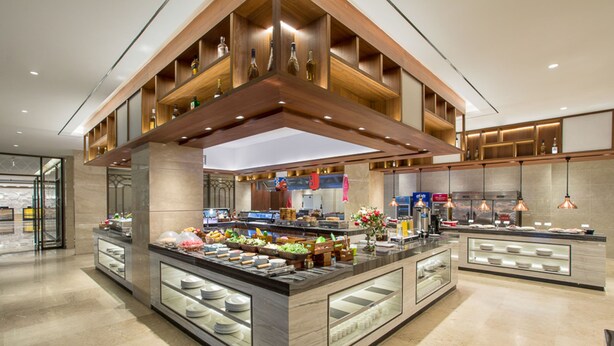 Una cocina moderna de hotel con una isla central, vitrinas de vidrio y estantes de madera.
