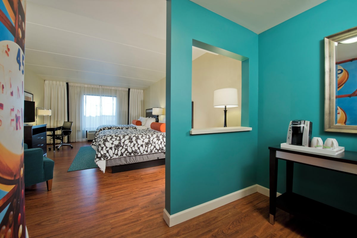 A hotel room with a bed, desk, chair, and a coffee machine.