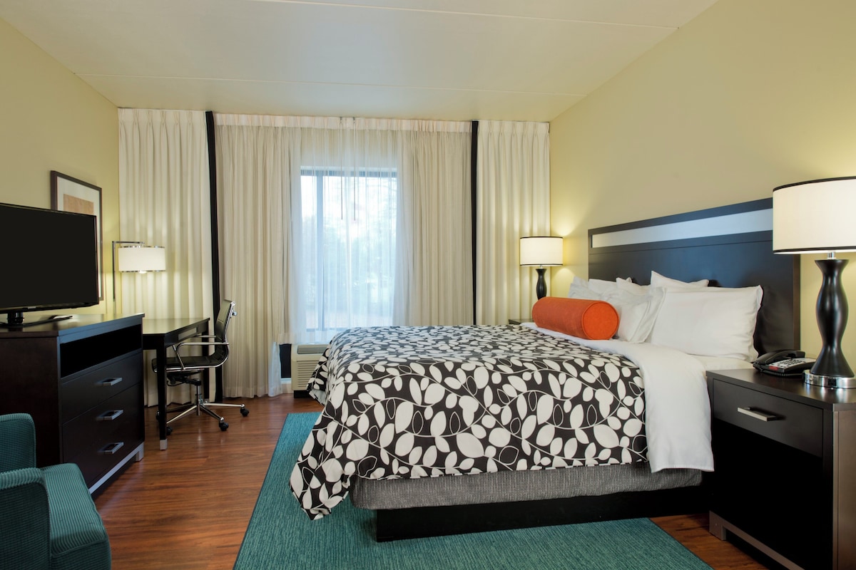 A hotel room with a bed, desk, chair, television, and lamps.