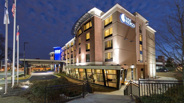 Hotel com design moderno, destacando uma entrada imponente com galeria coberta, vários andares e um mastro com bandeiras.