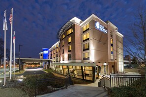 A hotel with a modern design, featuring a prominent entrance with a covered walkway, multiple floors, and a visible flagpole with flags. - Hotel Indigo Atlanta Airport - College Park by IHG (College Park)