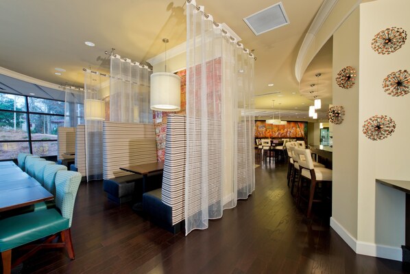 Un restaurante moderno con mesas altas, cabinas y un área de bar, además de decoración en las paredes.