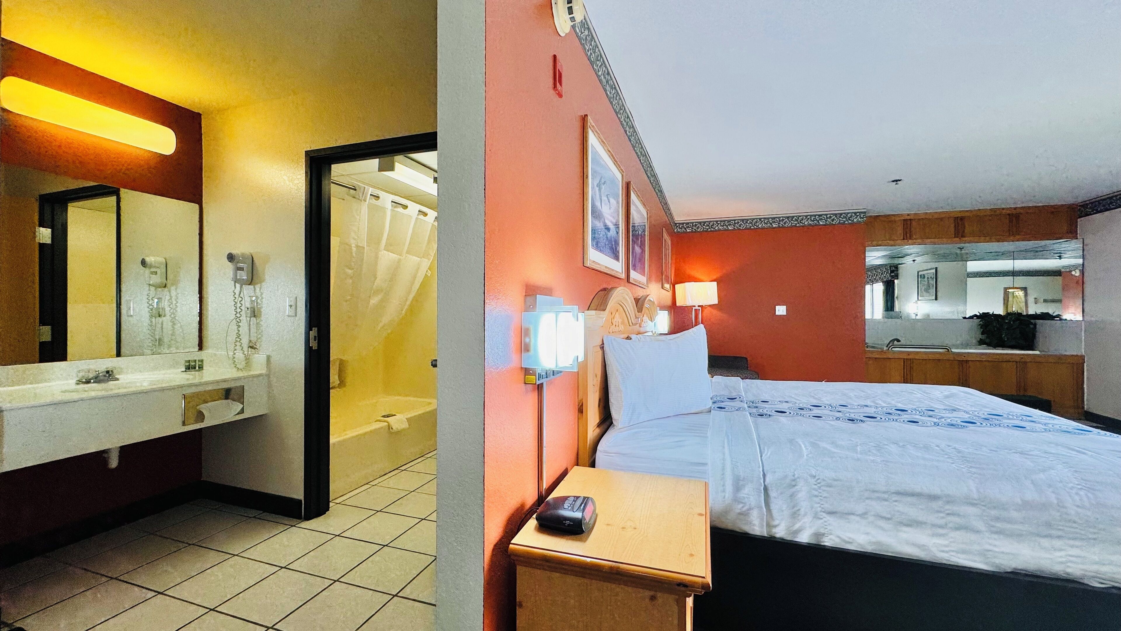 A hotel room with a bed, bedside table, and a bathroom with a shower and toilet.