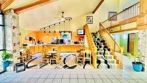 A spacious lobby with a central bar area, wooden staircase, and stone walls.