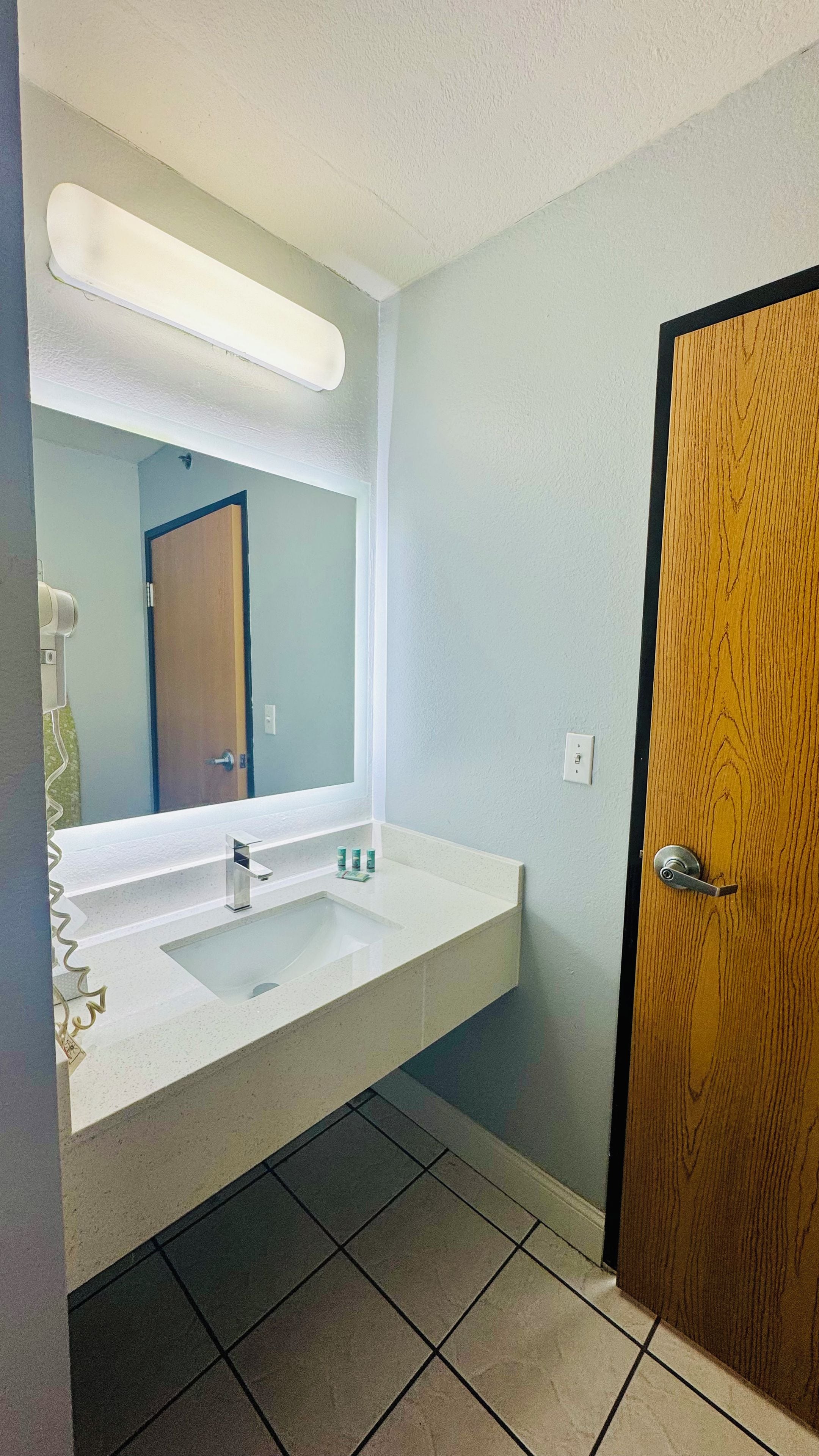Un baño con un lavamanos blanco, un espejo y una puerta de madera.