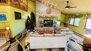 A cozy living room with a stone fireplace, a sofa, a coffee table, and a ceiling fan.