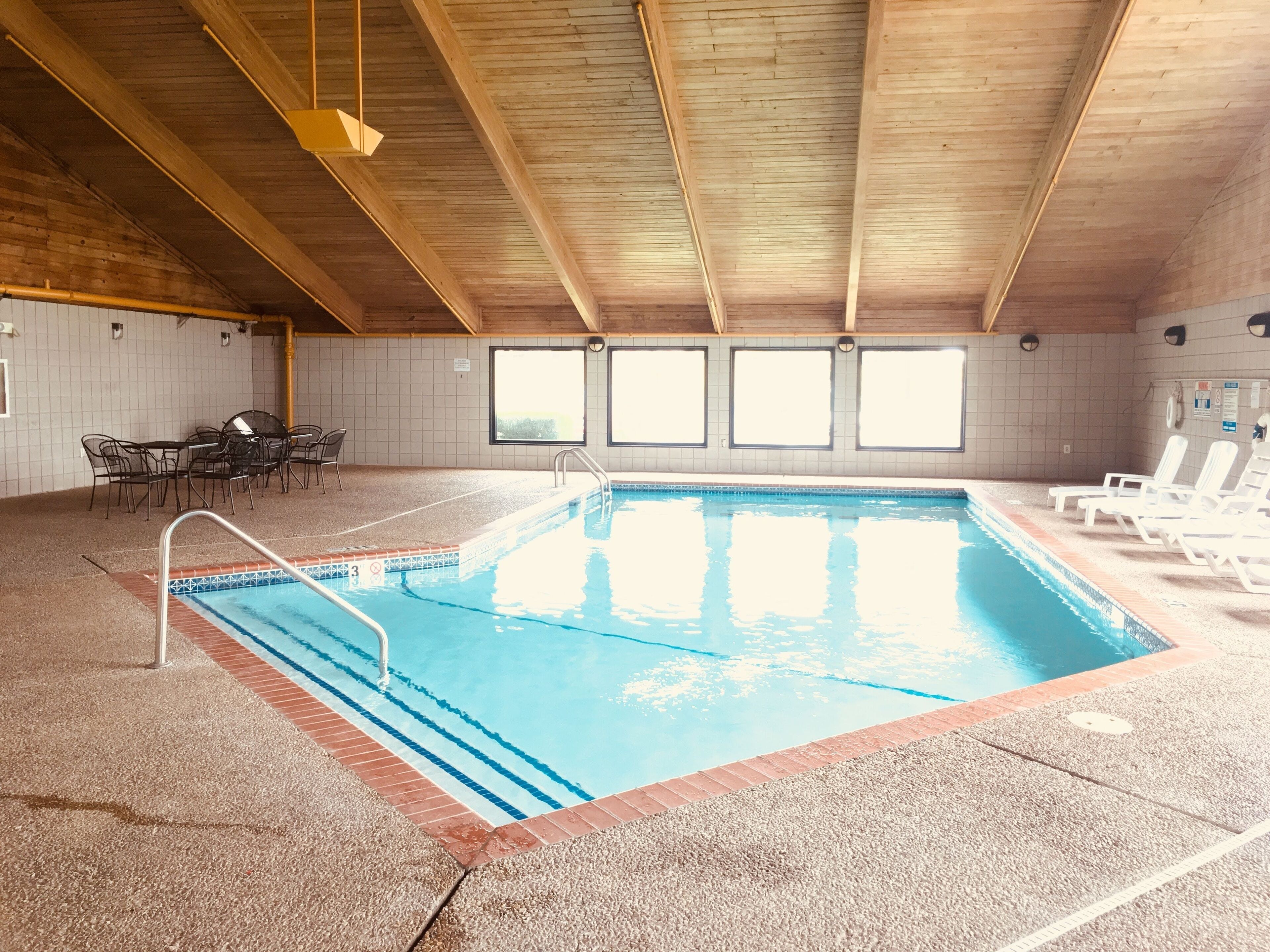 Una piscina interna con soffitto in legno, pareti piastrellate e una zona relax con sedie e tavoli.