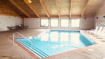 Una piscina interna con soffitto in legno, pareti piastrellate e una zona relax con sedie e tavoli.