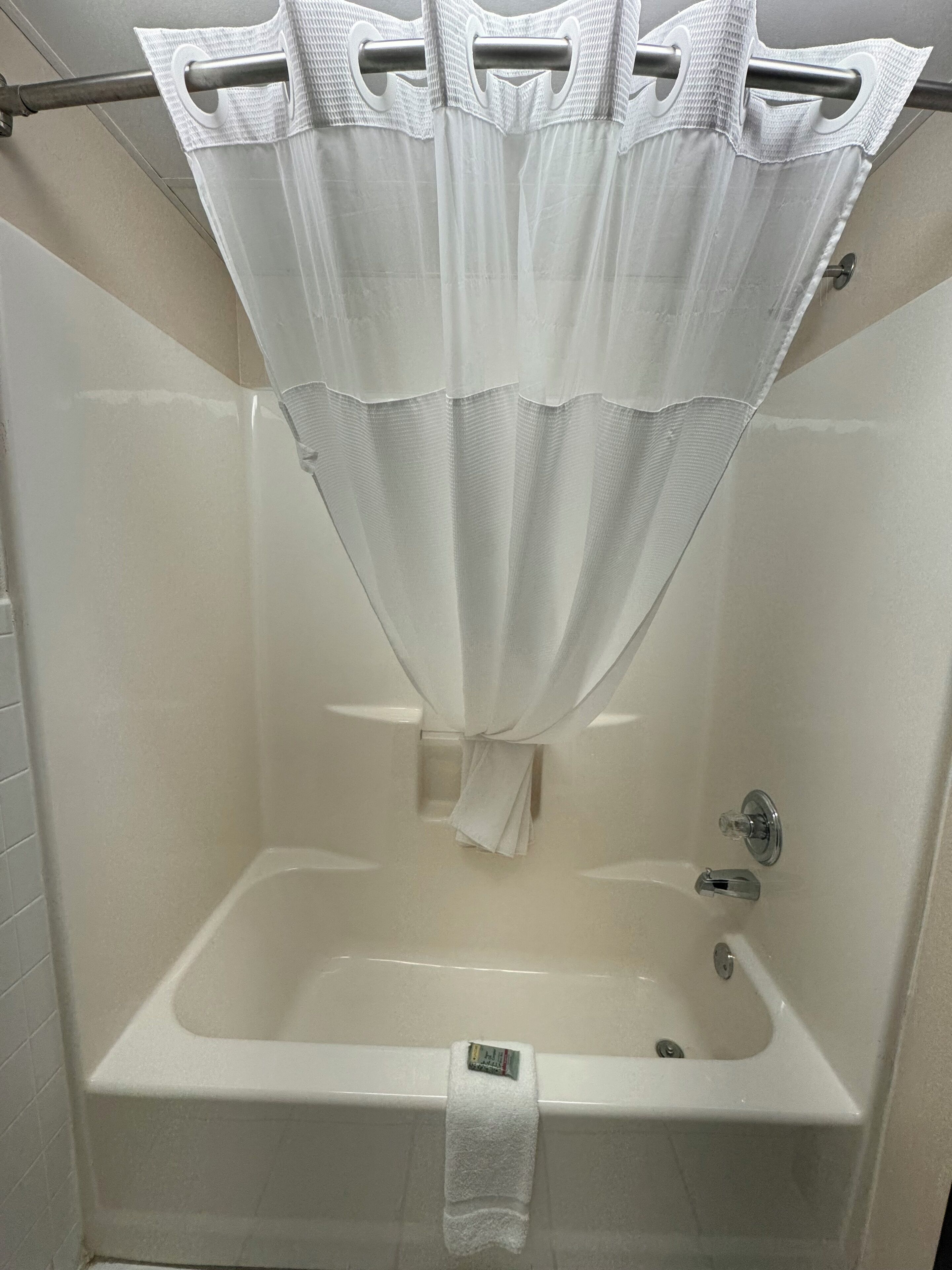 A white bathtub with a shower curtain, a towel hanging on the side, and a soap dispenser on the wall.