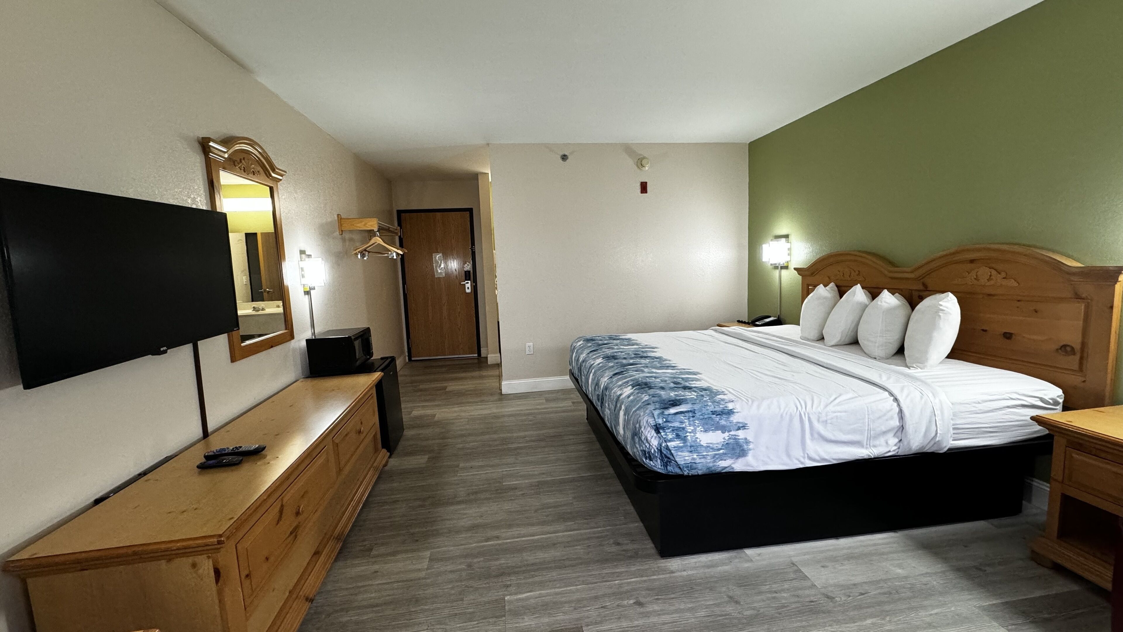 A hotel room with a bed, a TV, a dresser, and a mirror.