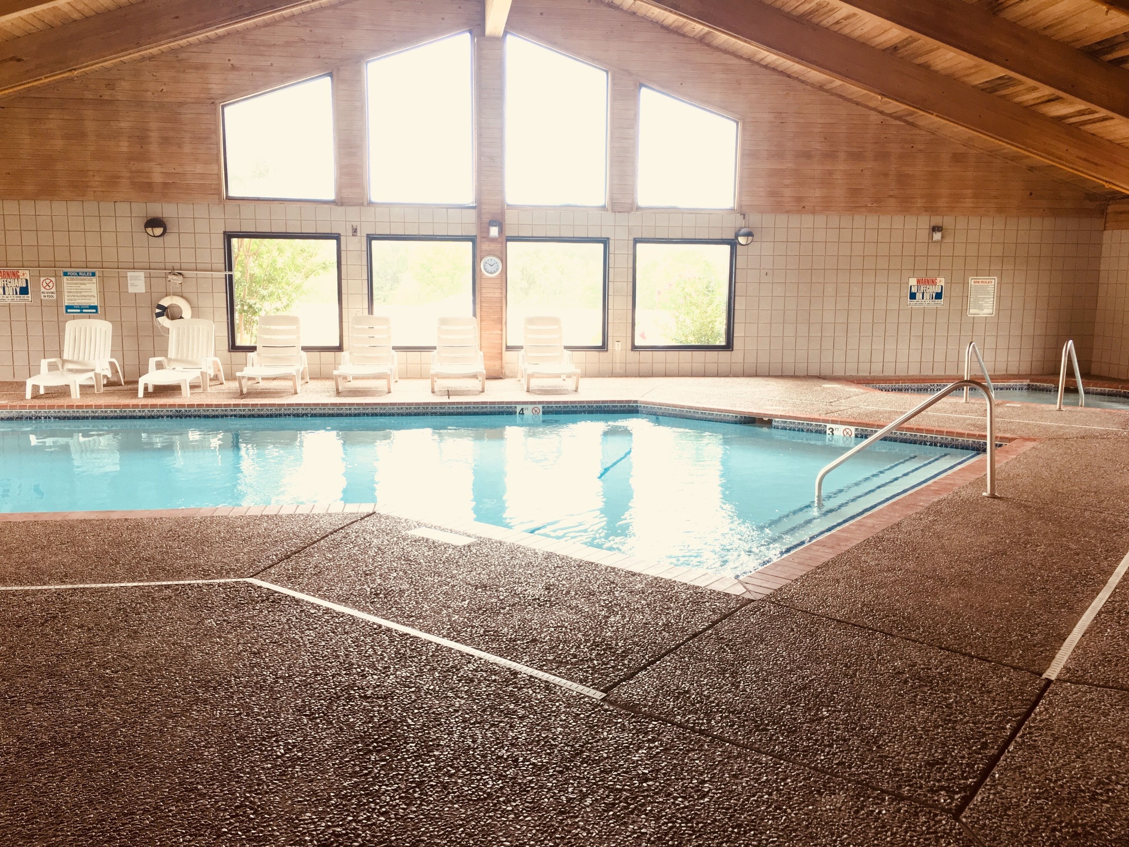 An indoor swimming pool with clear water, surrounded by white lounge chairs and a tiled floor.