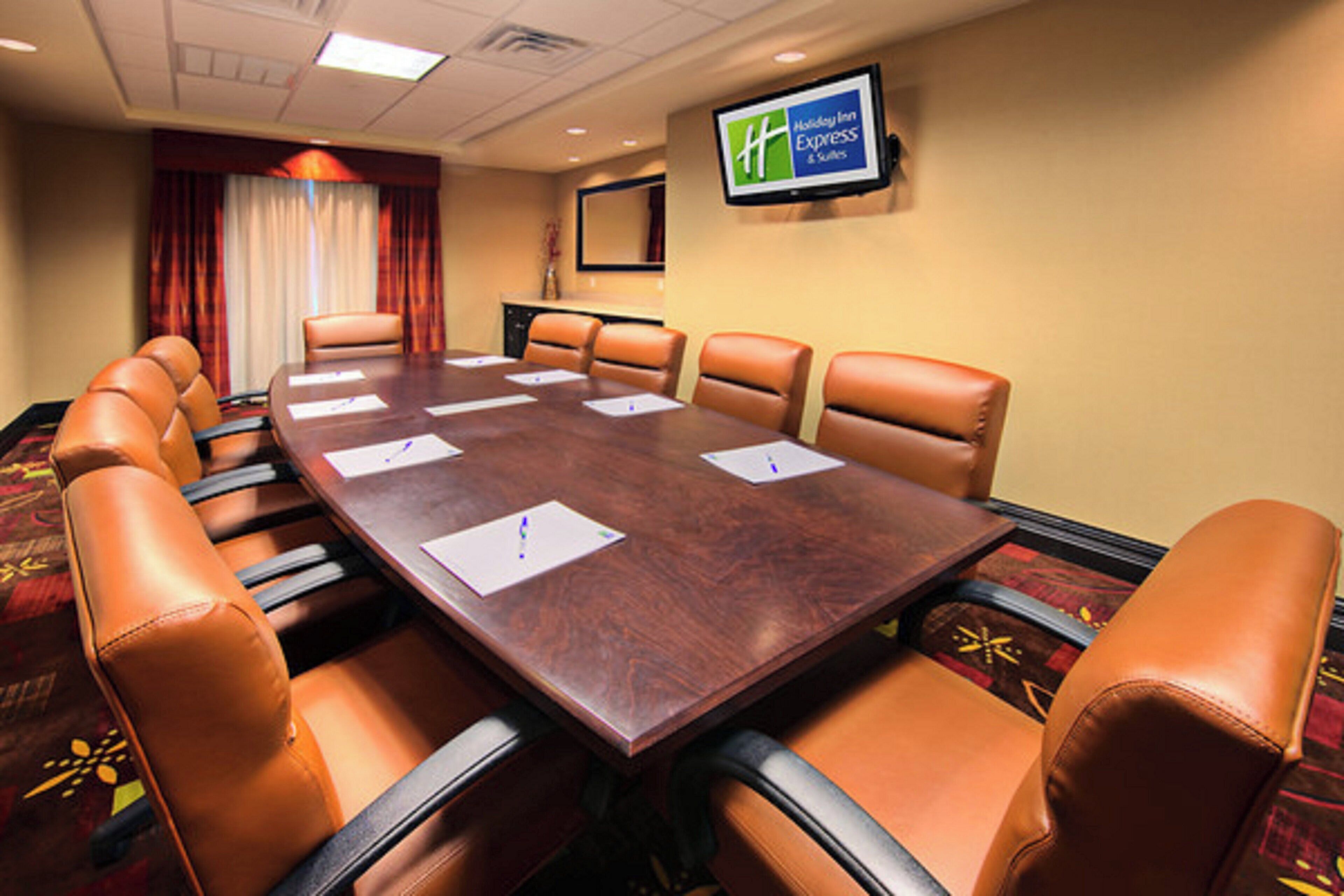 A conference room with a long table, six chairs, and a television on the wall.