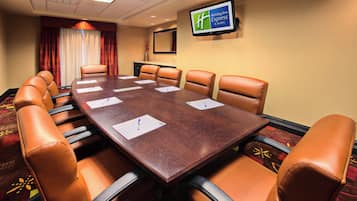 A conference room with a long table, six chairs, and a television on the wall.
