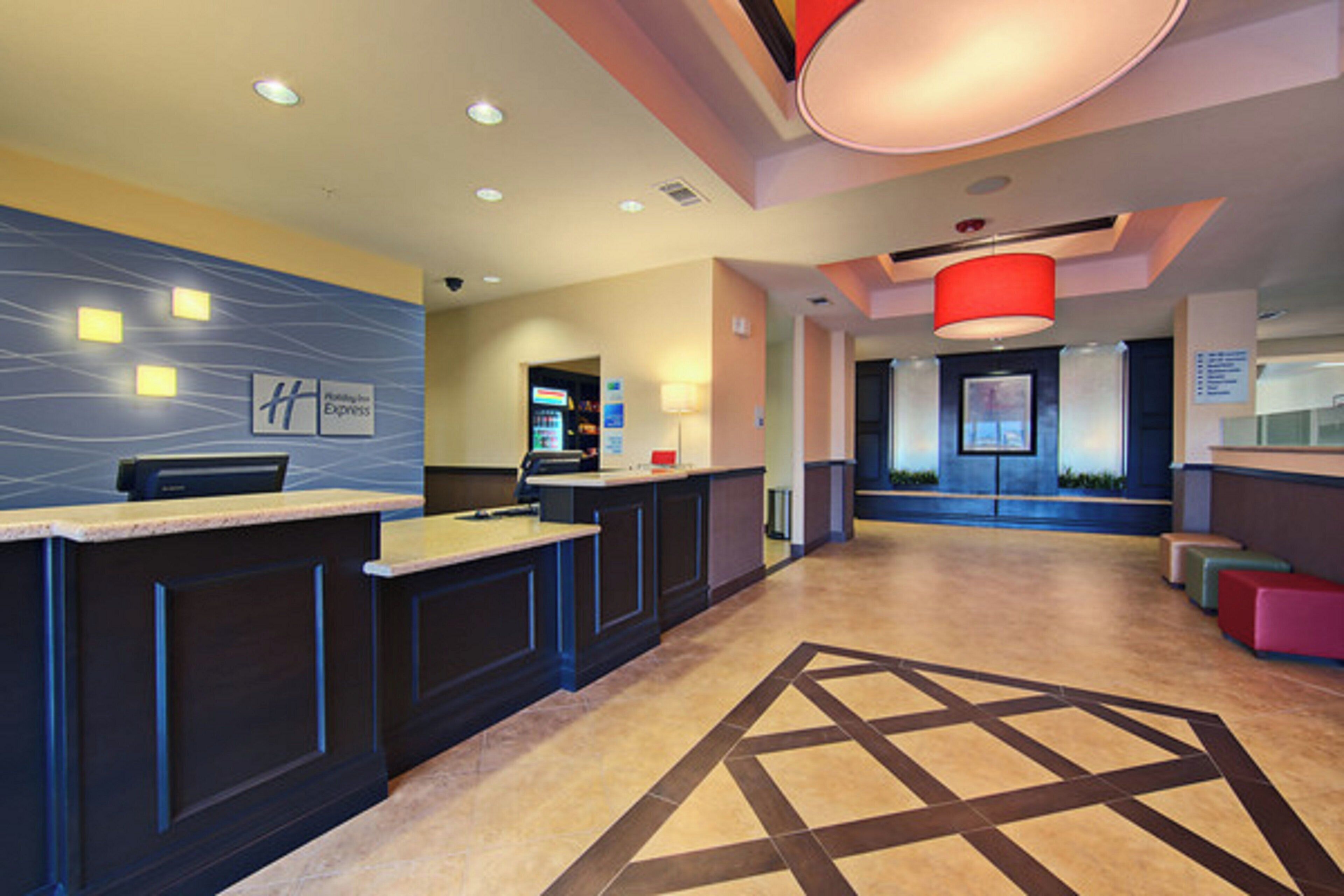 A hotel reception area with a reception desk, a digital display, and a seating area with a patterned floor.