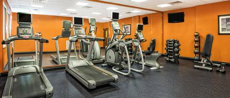 Un gimnasio con cintas de correr, elípticas y equipo de levantamiento de pesas.