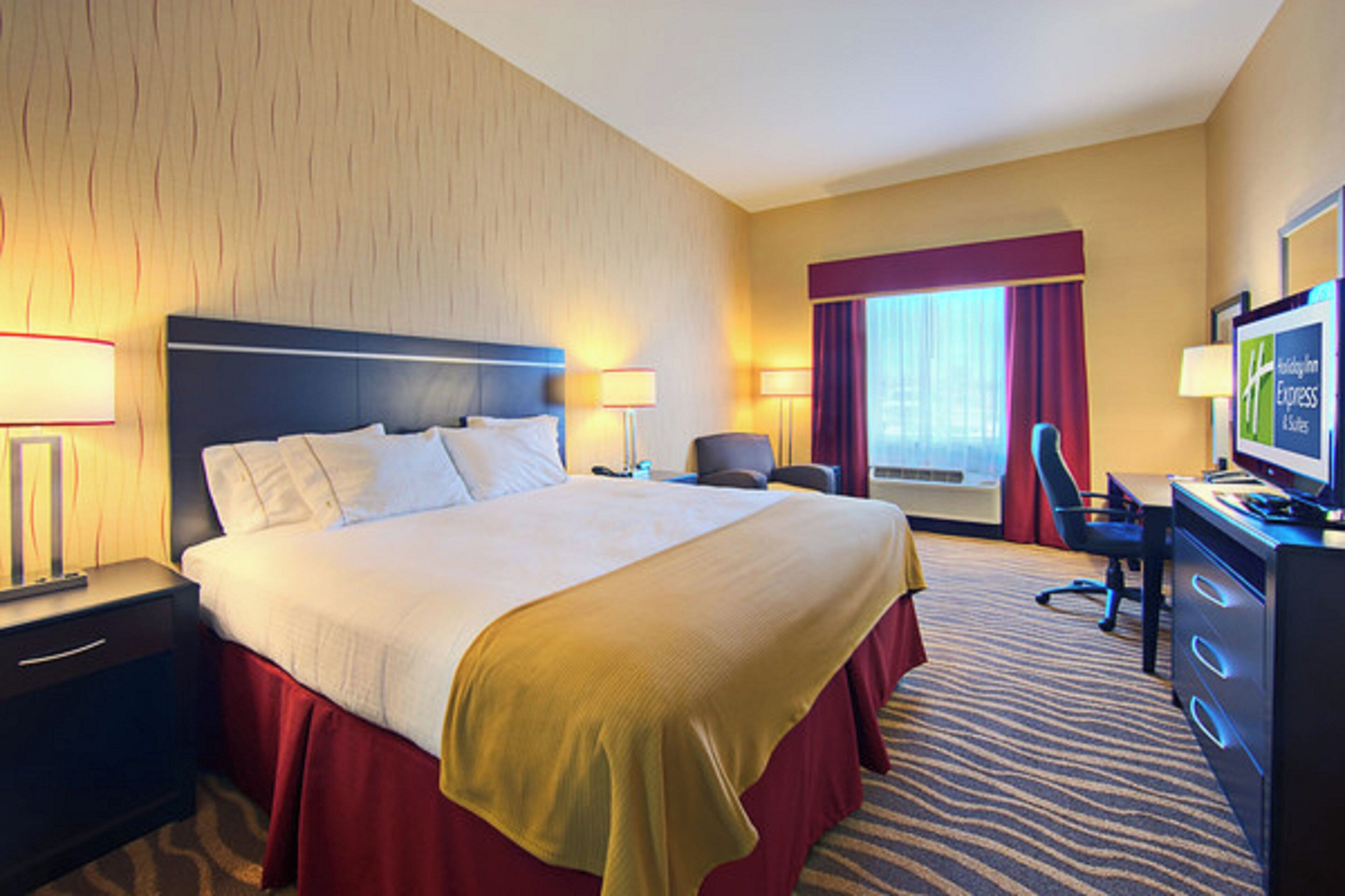 A hotel room with a large bed, a desk with a computer, a chair, and a television.