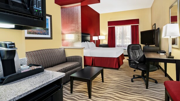 A hotel room with a bed, a sofa, a desk, a chair, a coffee maker, a TV, and a microwave. - Holiday Inn Express & Suites Cotulla by IHG (Cotulla)