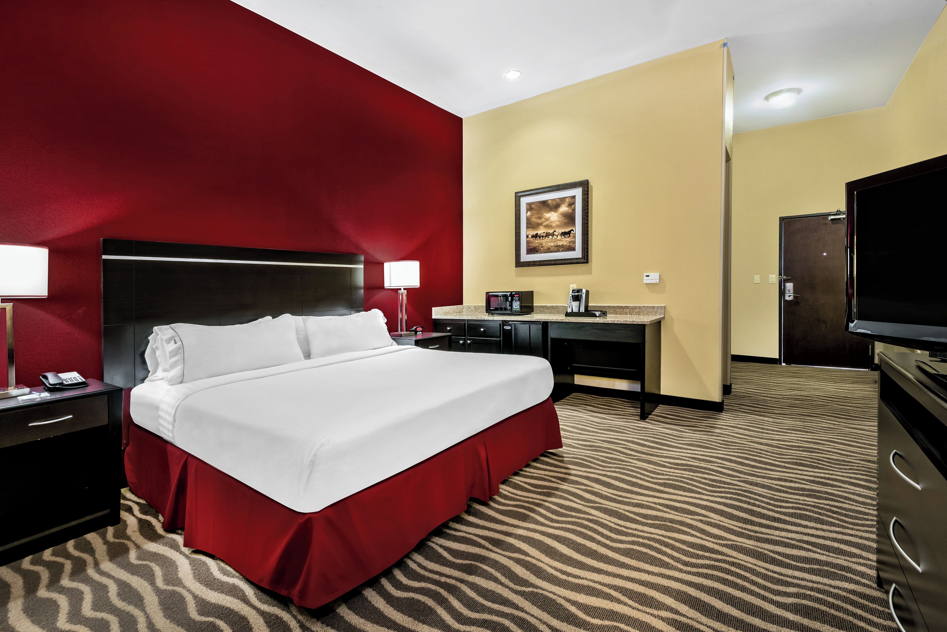 A hotel room with a large bed, a desk, a television, and a microwave.