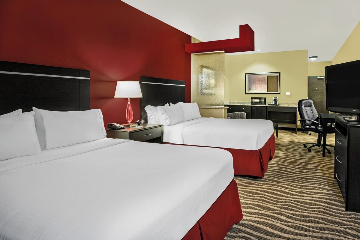 A hotel room with two beds, a desk, a chair, a TV, and a mirror.