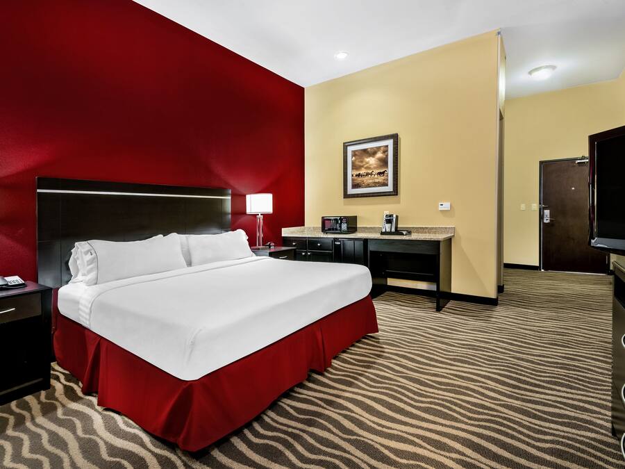 Une chambre d’hôtel avec un grand lit, un bureau, une télévision et un mur d’accent rouge.