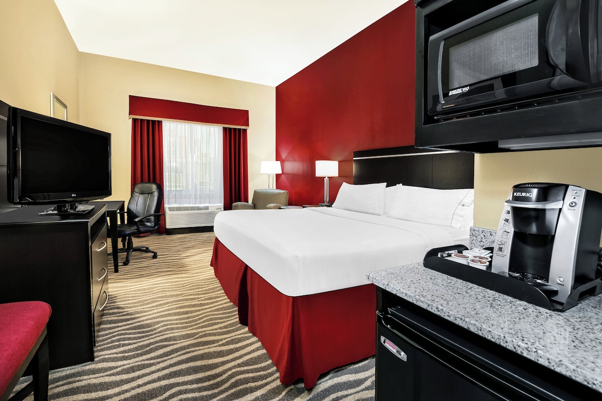 A hotel room with a bed, desk, television, coffee maker, and a view of the city.