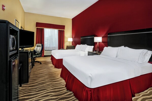 A hotel room with two beds, a desk with a television, a chair, a desk lamp, and a red carpet.