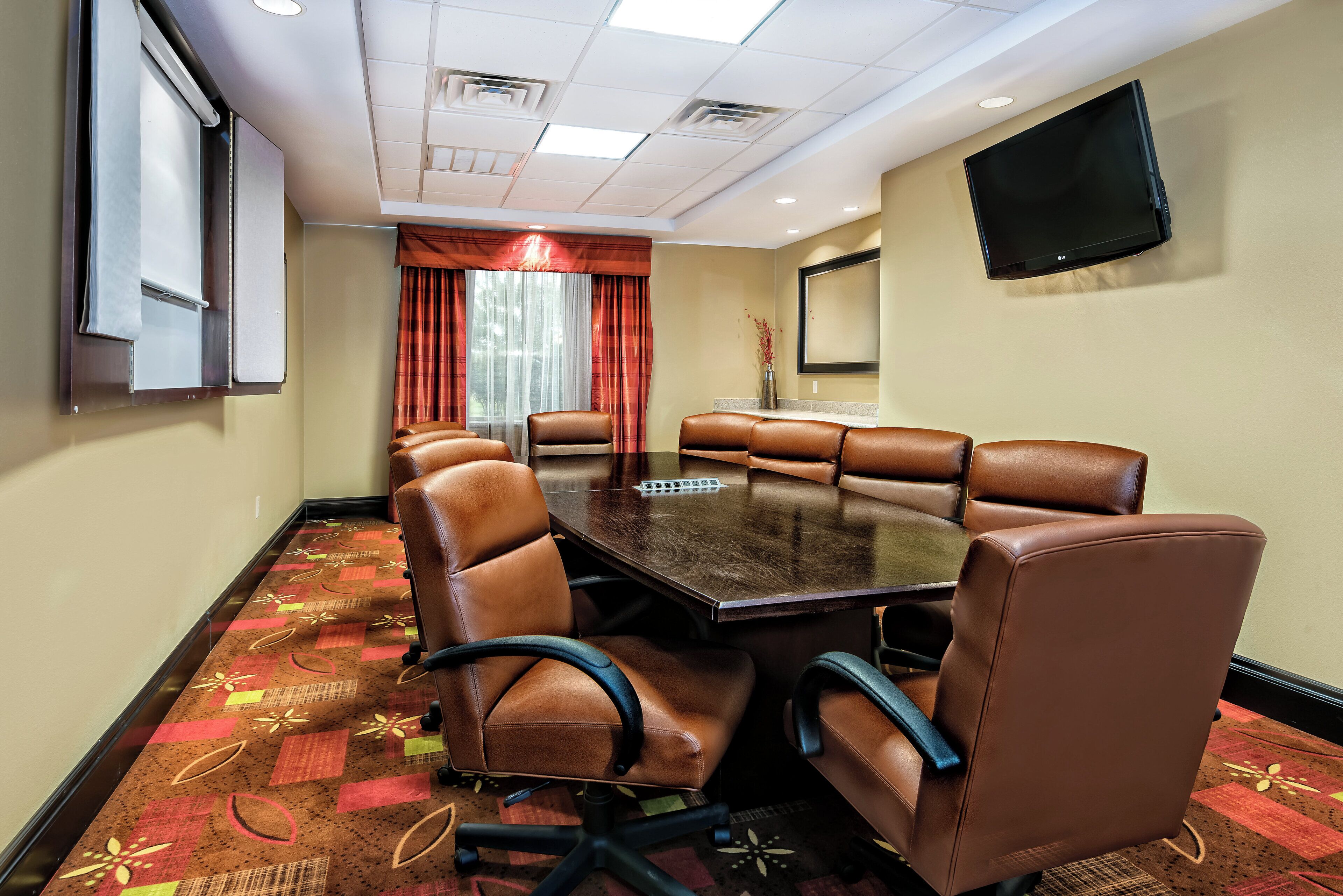 A conference room with a large table, leather chairs, a flat-screen TV, and a projector screen.