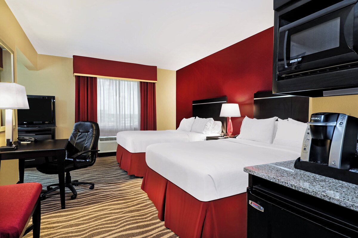 A hotel room with two beds, a desk with a chair, a TV, a coffee maker, and a microwave.