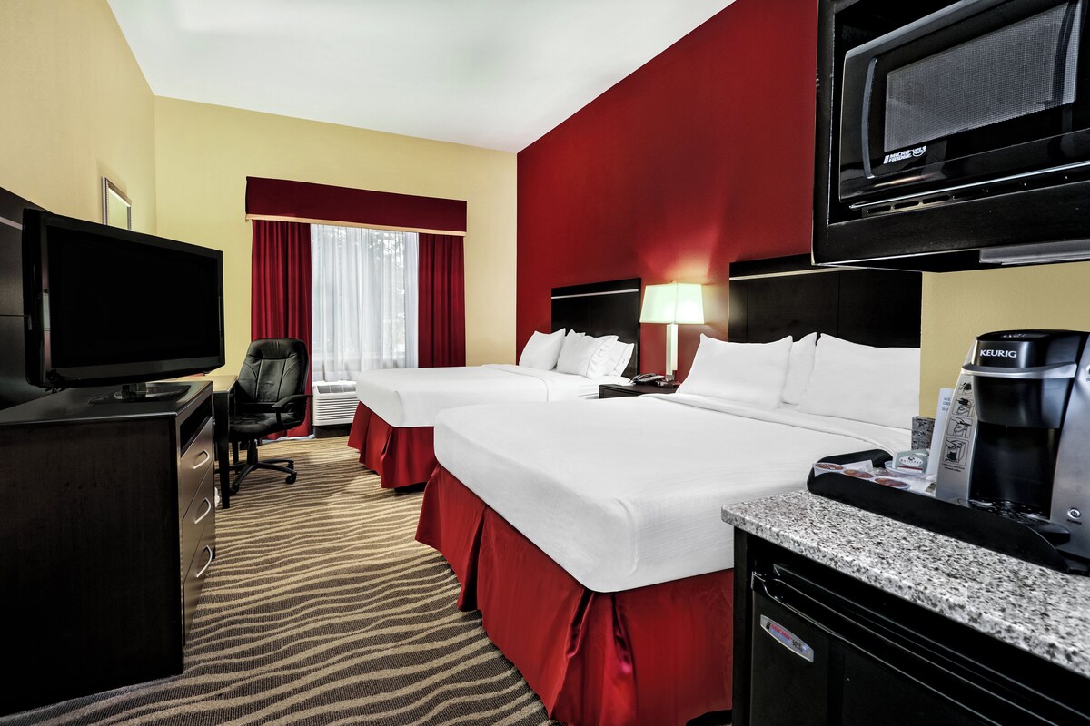 A hotel room with two beds, a desk with a TV, a coffee maker, and a window with curtains.