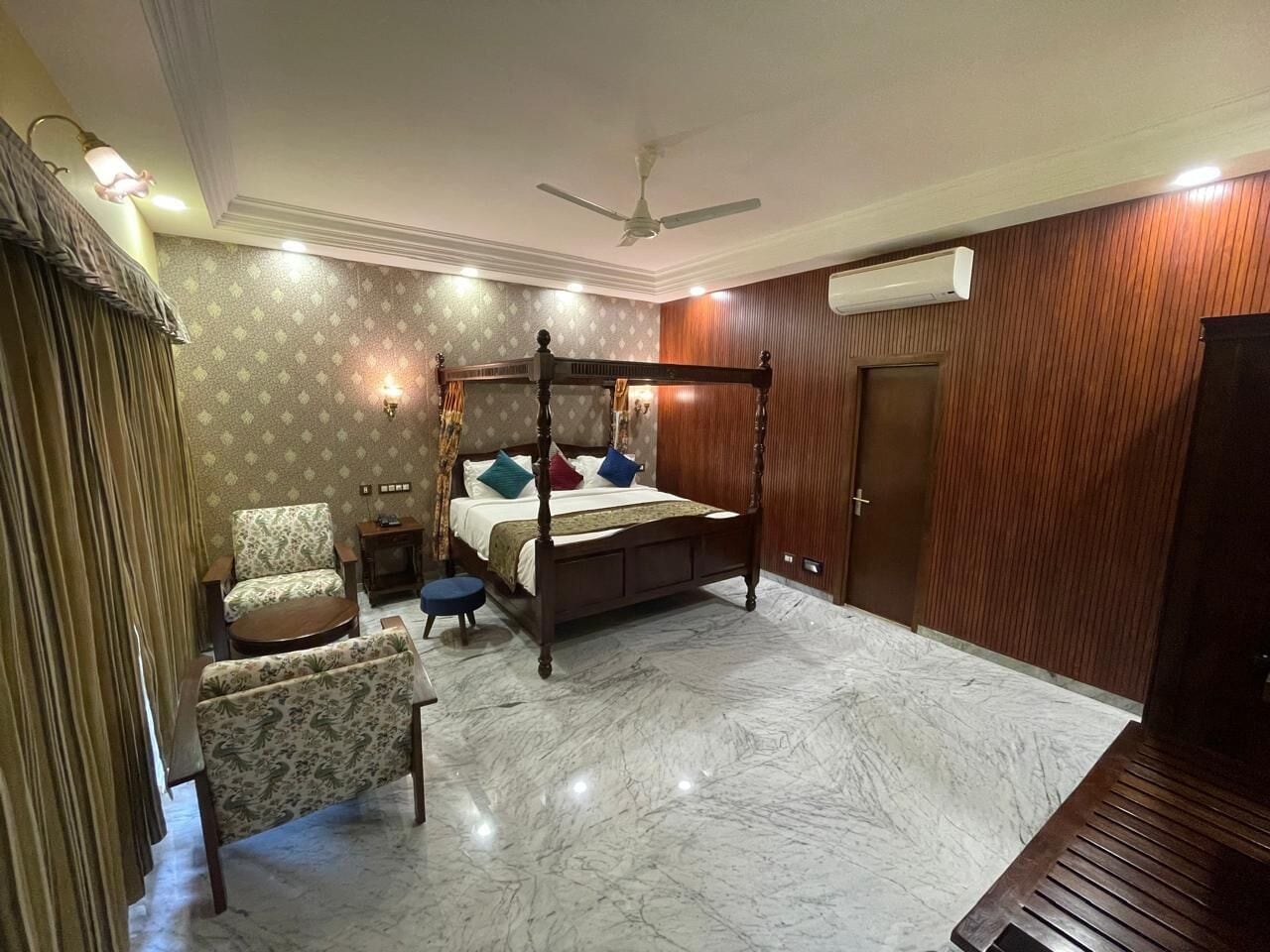 Un dormitorio con una cama con dosel, una silla, una mesita y un ventilador de techo.