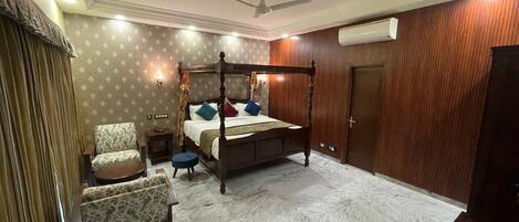 Un dormitorio con una cama con dosel, una silla, una mesita y un ventilador de techo.