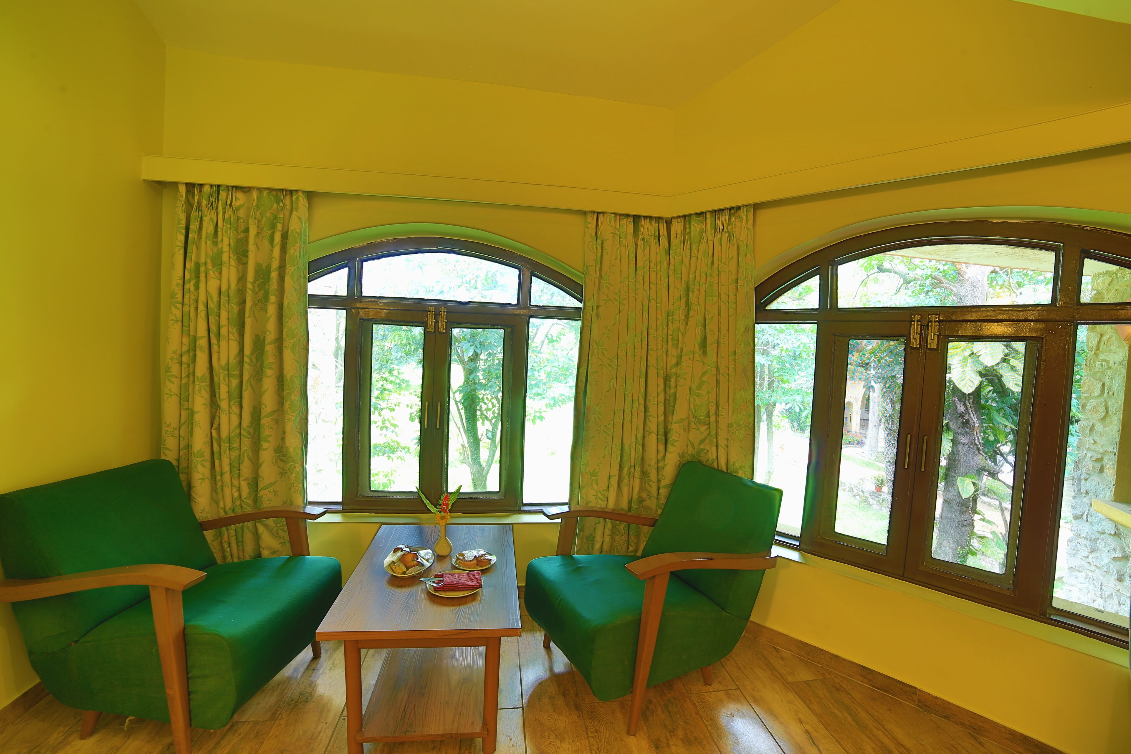 A room with two green chairs, a wooden table, and a window with curtains.