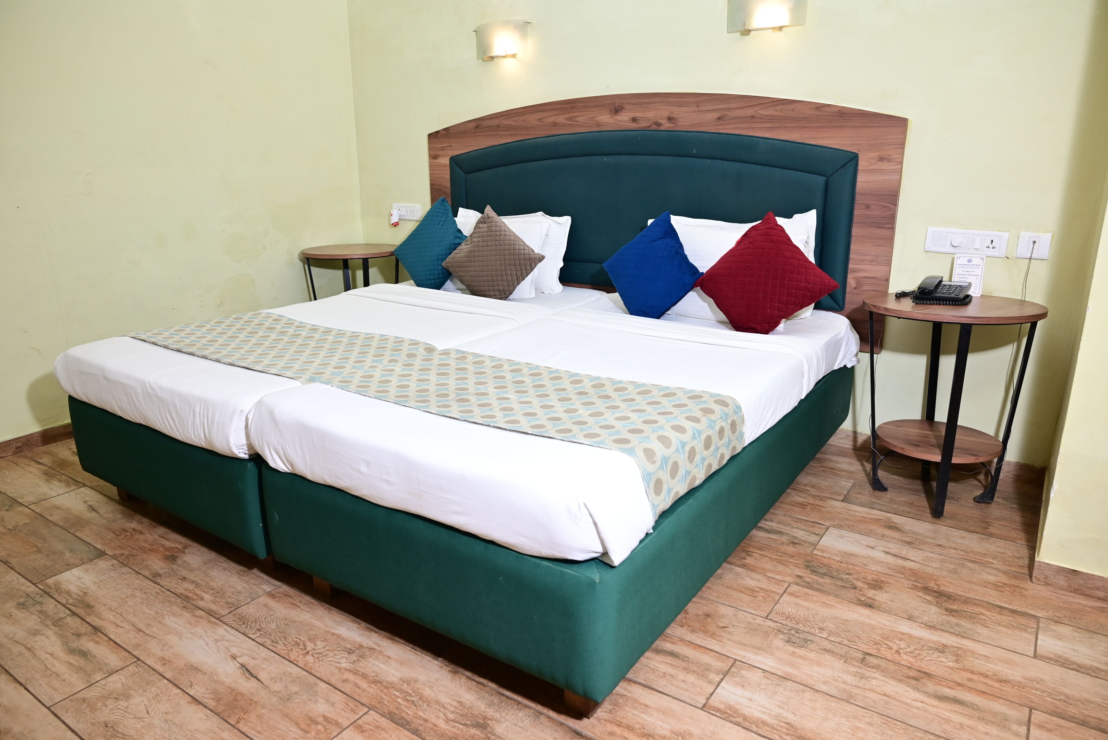A neatly made bed with a wooden headboard, a bedside table with a phone, and a wall socket.
