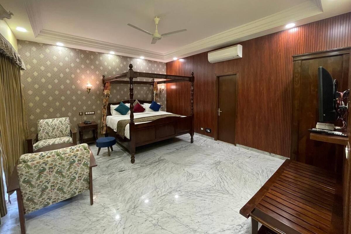 A bedroom with a four-poster bed, a wooden wardrobe, a small bedside table, a chair, and a bench.
