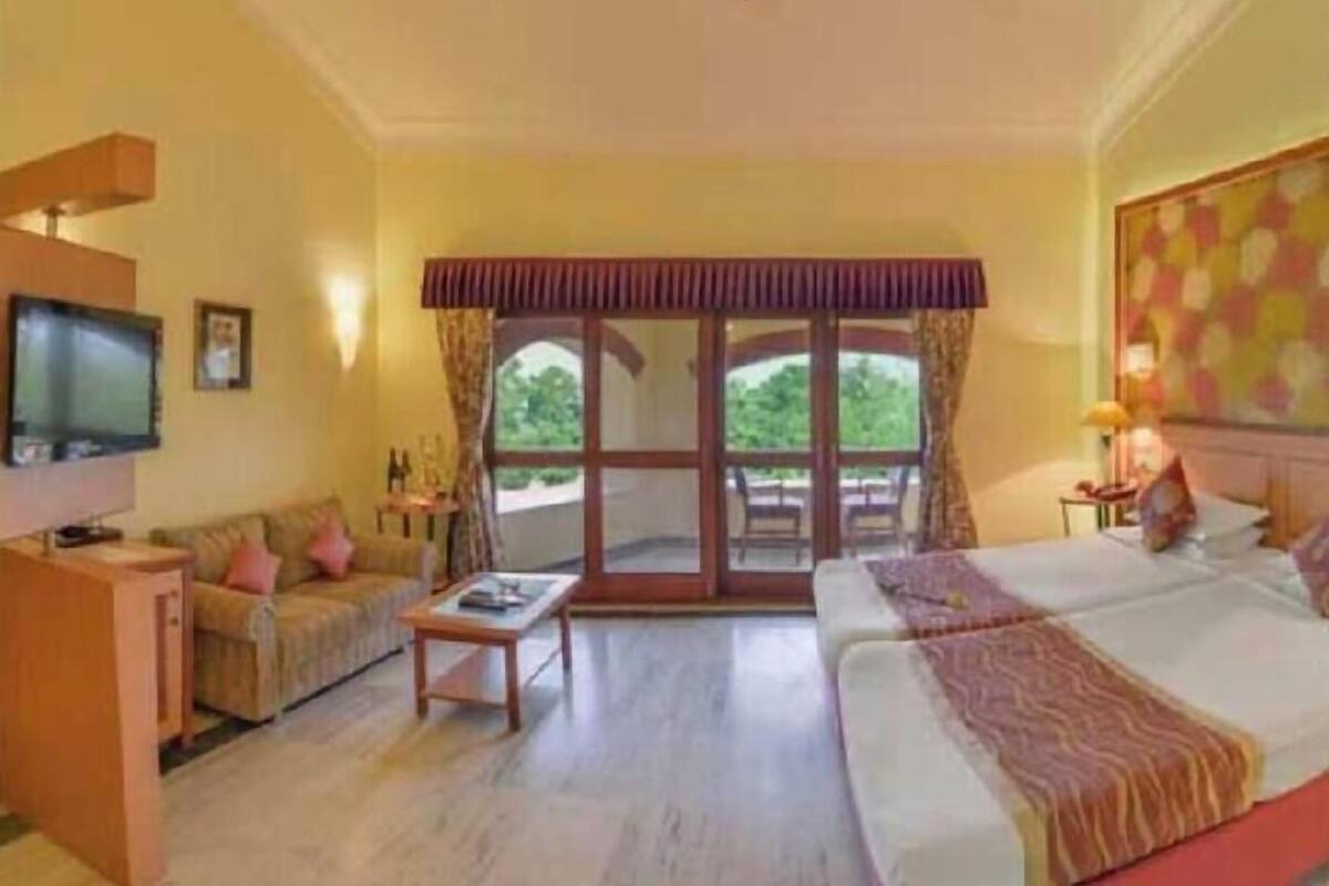A hotel room with a sofa, a bed, a television, and a large window.