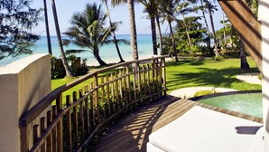A wooden deck with a white cushioned seating area overlooking a pool and palm trees. - Ajinta Resort (Ko Kood)