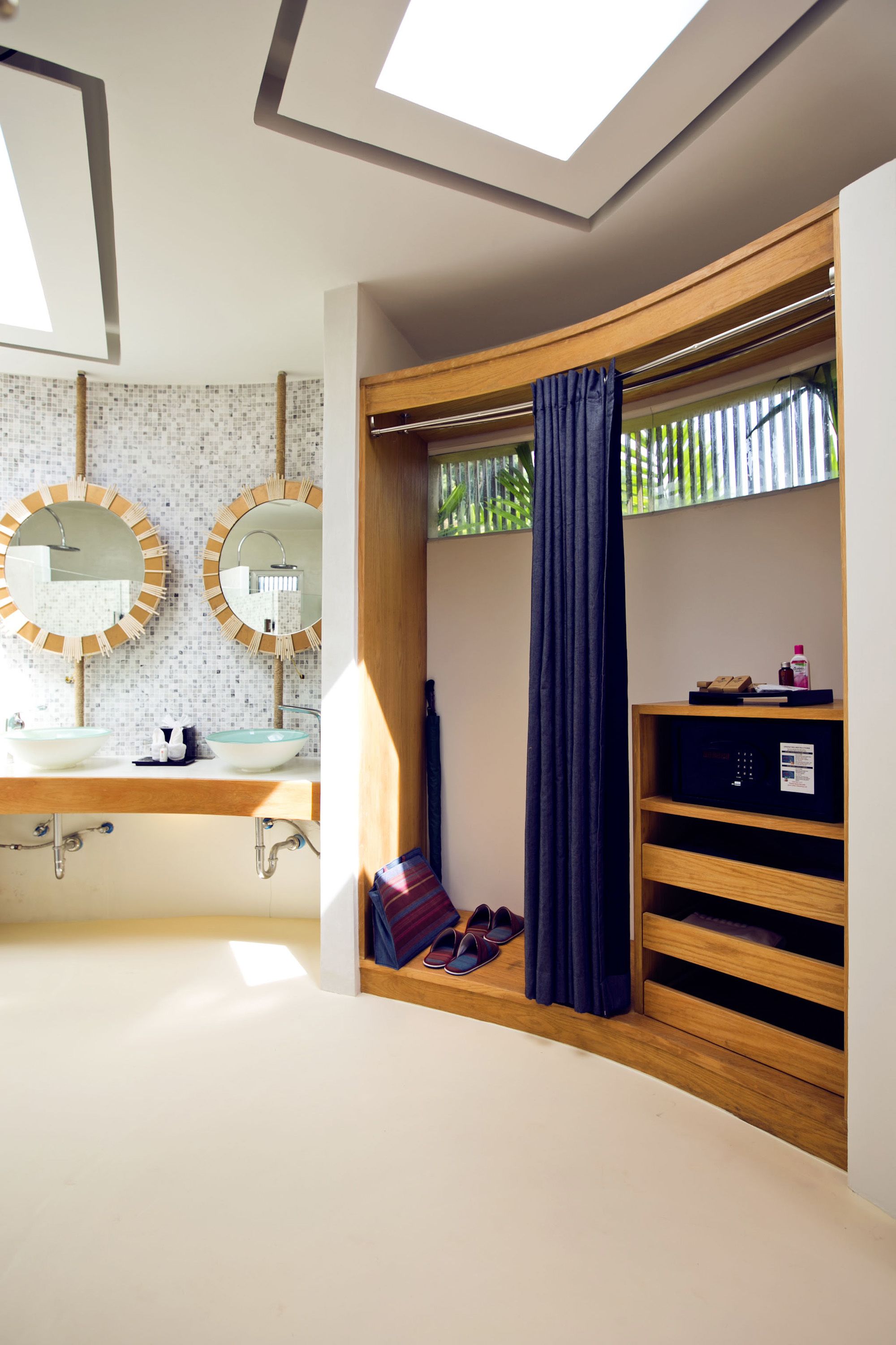 Een moderne badkamer met dakramen, een wastafel met twee spiegels, een douchegedeelte en een houten plank met een handdoek en slippers.