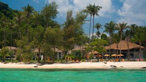 A beach resort with clear turquoise waters, palm trees, and beach umbrellas. - Ajinta Resort (Ko Kood)