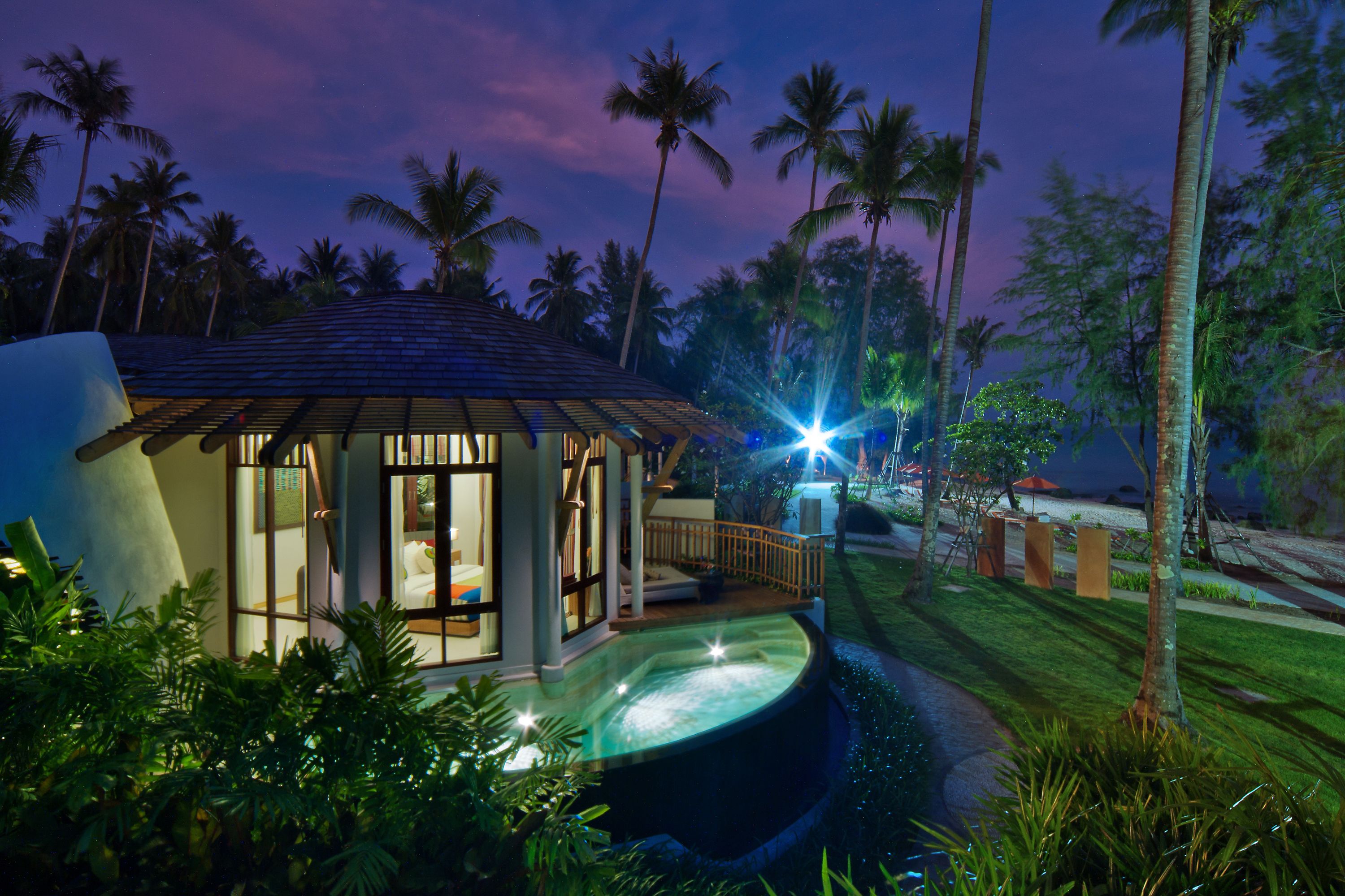 A resort with a pool, palm trees, and a well-lit building.