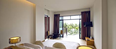 Una habitación de hotel moderna con una cama grande, dos mesitas de noche con lámparas, un televisor de pantalla plana y un balcón con vistas a palmeras.