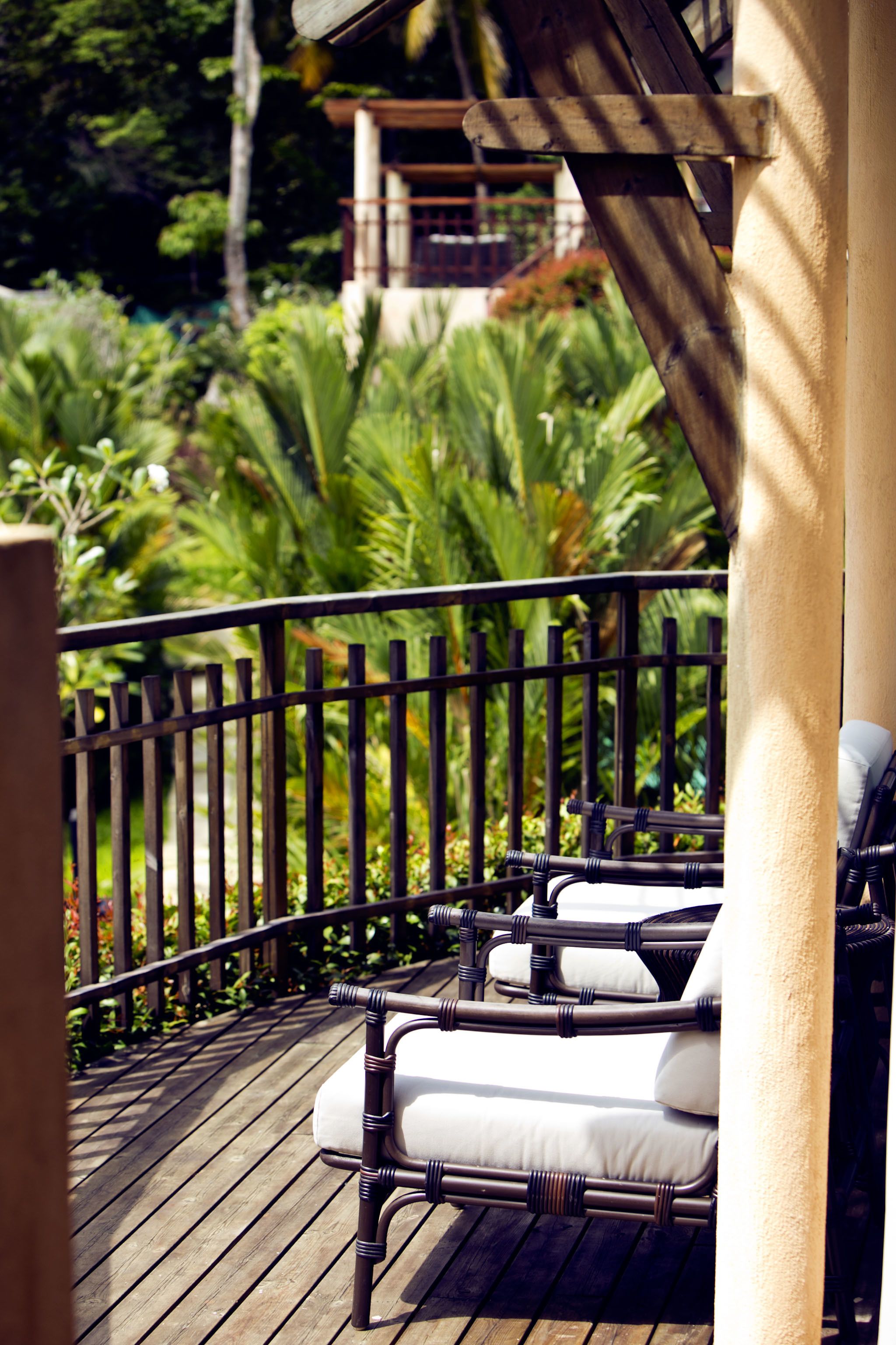 A wooden deck with a black metal railing, white cushioned chairs, and lush greenery in the background.