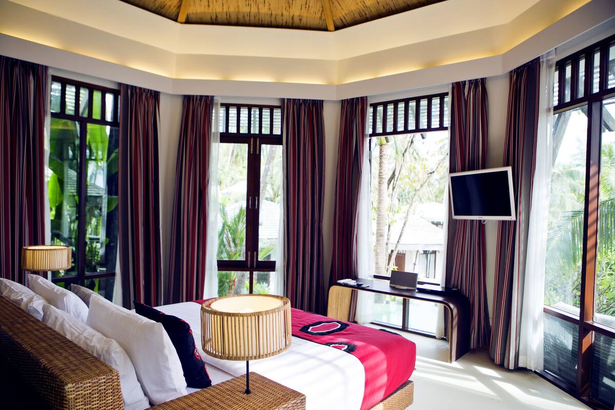 A hotel room with a bed, a desk, a TV, and large windows with curtains.