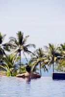 Un hombre en una piscina con vista a palmeras y al océano.