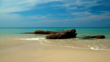 Une plage avec une eau turquoise et limpide, et de gros rochers au premier plan.