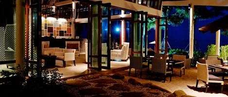 Un espacio de estar interior y exterior con vista al cielo nocturno y palmeras.