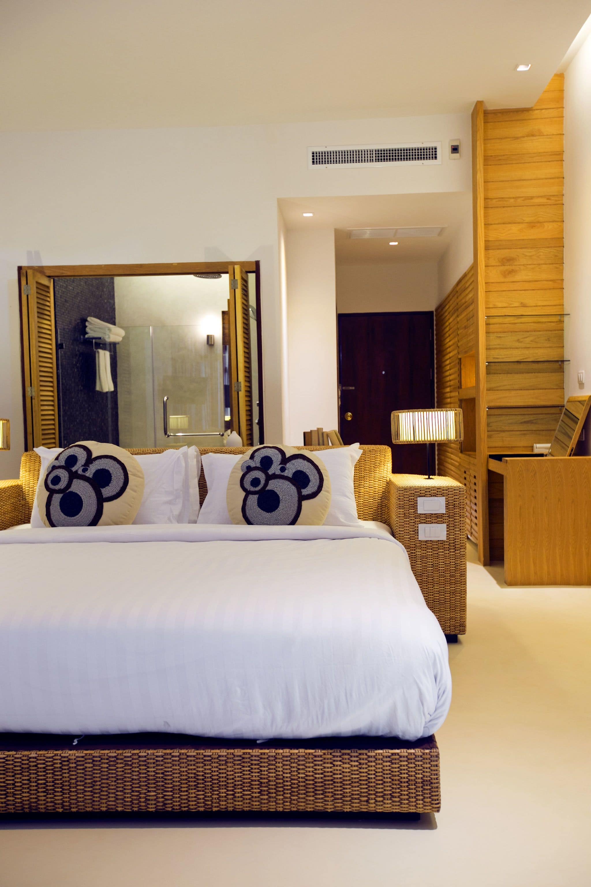 A modern hotel room with a large bed, a wooden wardrobe, a mirror, and a bathroom visible through an open door.