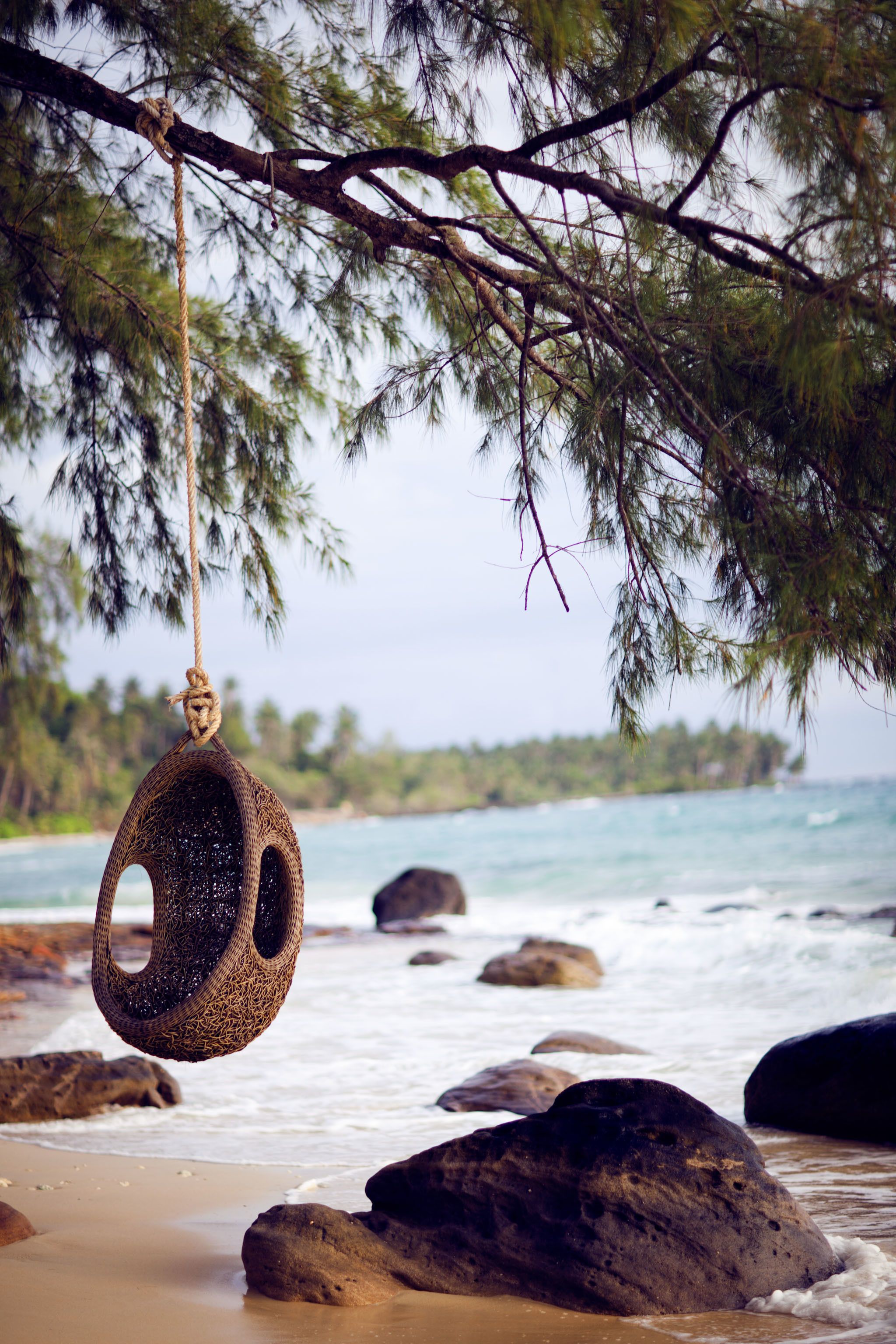 A beach scene with a hanging tire swing, rocks, and the ocean.
