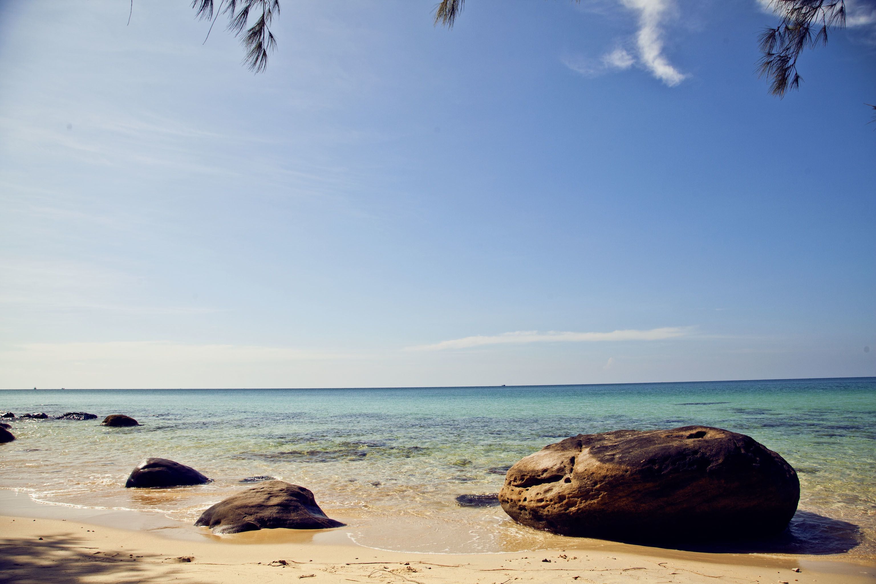 Ein Strand mit klarem Wasser, großen Felsen und einem sandigen Ufer.